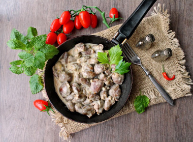 Stewed chicken hearts in sour cream in a frying pan with onions