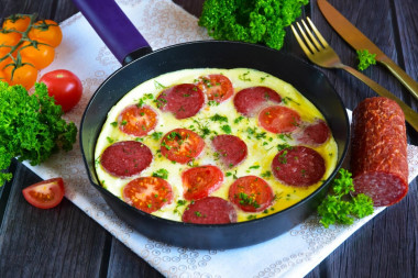 Omelet in a frying pan with sausage and tomatoes