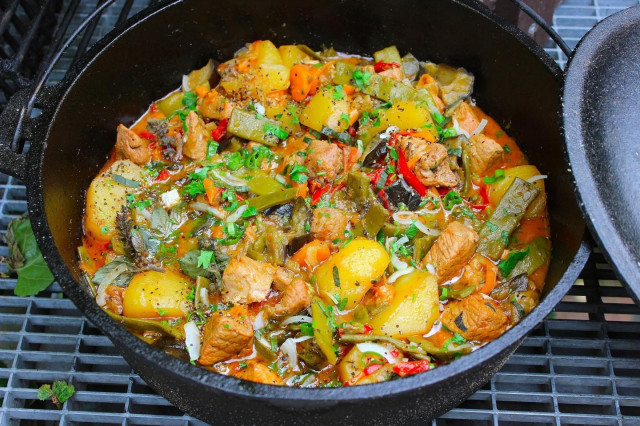 Vegetable stew in a cauldron with meat and potatoes on a campfire