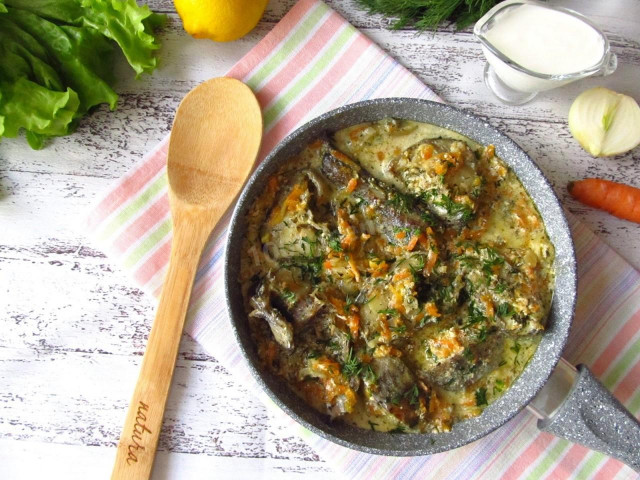 Pollock in sour cream filling in a pan with onions and carrots